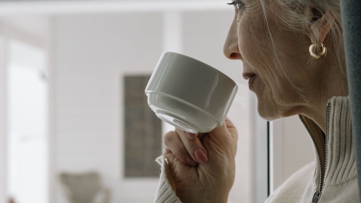 A silver-haired woman enjoys a calm cup of coffee by the window at home