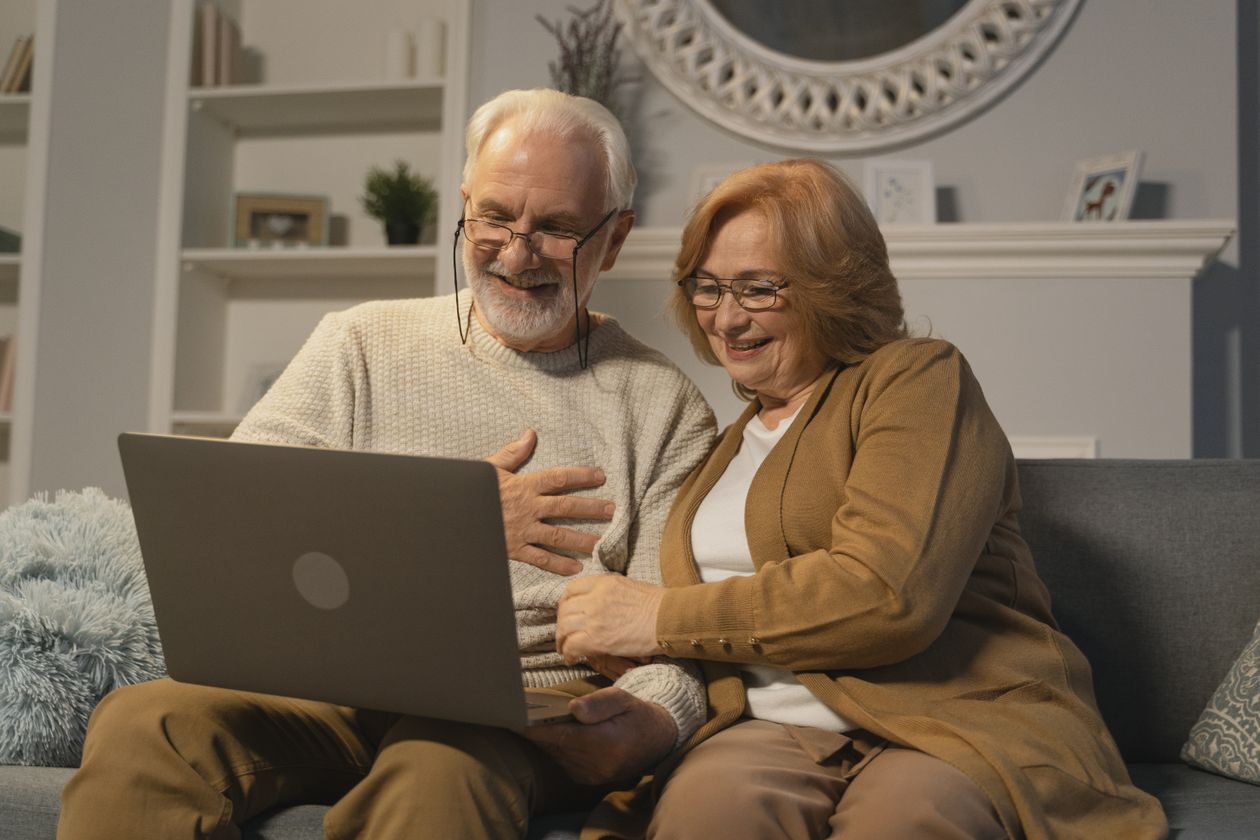 An older couple smile warmly during a video call with family on their laptop at home