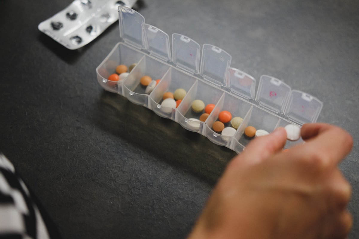 Eine Hand greift in eine Wochen-Pillenbox, um die Medikamente des Tages herauszunehmen